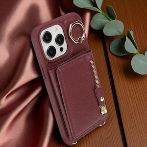 Puede incluir: Funda de teléfono burdeos con cartera y soporte de anillo. La funda tiene un aspecto de cuero texturizado, un soporte de anillo dorado y un bolsillo con cremallera. La funda está diseñada para un teléfono inteligente y tiene un recorte para la cámara.