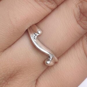 Peut inclure: Une bague en argent au design unique et fluide. La bague présente une bande incurvée avec une petite perle arrondie à chaque extrémité. La bague est portée au doigt, mettant en valeur son style élégant et minimaliste.
