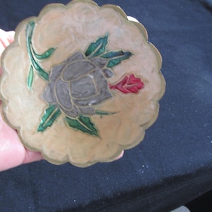 Peut inclure: Un plat décoratif à bord festonné avec un motif floral. Le plat présente un fond beige avec une rose grise, des feuilles vertes et un accent rouge. Le bord est de couleur or.