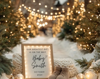 Puede incluir: Anuncio de embarazo con un letrero enmarcado que dice "OUR GREATEST GIFT IS ON THE WAY Baby Smith OCTOBER 202X." El letrero está iluminado con luces y está junto a un par de botines de bebé. El fondo es una escena nevada con luces navideñas.
