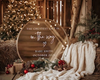 May include: A rustic pregnancy announcement scene with a round mirror displaying the text "THE GREATEST GIFT IS on the way" and the name "BABY SMITH OCTOBER 202X". The scene includes a Christmas tree, hay bales, a white blanket, pine cones, and red ornaments.
