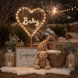 May include: A glowing heart-shaped light with the word "Baby". A sign reads "Our New Year Surprise" with "October 202X" below. A teddy bear sits near a wicker basket and a decorative lantern.