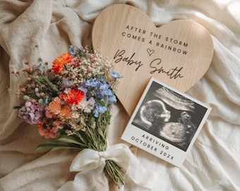 May include: A wooden heart-shaped sign with the text "AFTER THE STORM COMES A RAINBOW" and "Baby Smith". A bouquet of colorful flowers and a sonogram photo that reads "ARRIVING OCTOBER 202X" are also present.