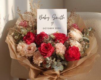 May include: A bouquet of red roses and peach-colored carnations wrapped in brown paper. A white card with the text "Baby Smith" and "October 202X" is placed in the center of the flowers. The bouquet is tied with a cream ribbon.