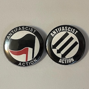 May include: Two circular badges with the words "ANTIFASCIST ACTION". One has a black flag with a red detail, the other has three downward-pointing arrows, all on a black and white background.