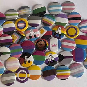Peut inclure: Une collection de badges ronds et colorés avec divers motifs et motifs. Les badges présentent des rayures, des drapeaux et des symboles représentant différentes identités et causes. Les badges sont dispersés sur une surface blanche.