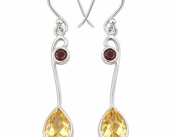 Puede incluir: Un par de pendientes colgantes de plata con un diseño de metal curvado. Cada pendiente tiene una pequeña piedra preciosa redonda de color rojo oscuro en la parte superior y una piedra amarilla más grande, facetada y en forma de pera abajo.