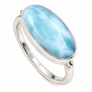 Könnte beinhalten: Ein Silberring mit einem großen, ovalen, hellblauen Larimar-Edelstein in einer glatten Fassung. Der Ring aus poliertem Silber trägt auf der Innenseite einen deutlich sichtbaren 925-Stempel, der auf die Zusammensetzung aus Sterlingsilber hinweist.