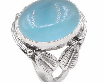 May include: A silver ring featuring a large, smooth, oval-shaped light blue cabochon stone set in a polished metal bezel. The band is decorated with two pairs of detailed, textured leaf motifs on either side, extending from the central setting.