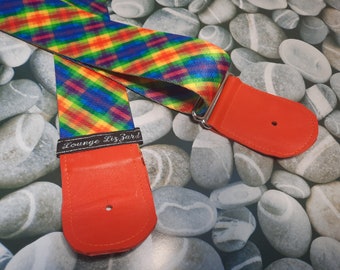 May include: A rainbow plaid guitar strap with red leather ends. The strap has the text "Lounge Lizard" printed on it.