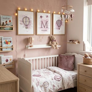 Peut inclure: Un lit à barreaux blanc avec une parure de lit à motifs de montgolfières, trois cadres muraux illustrant des montgolfières et la lettre M, un mobile suspendu avec des nuages et des ballons, un ours en peluche et des guirlandes lumineuses.