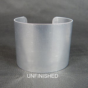 May include: Unfinished silver metal cuff bracelet. The bracelet is smooth and has a brushed finish.