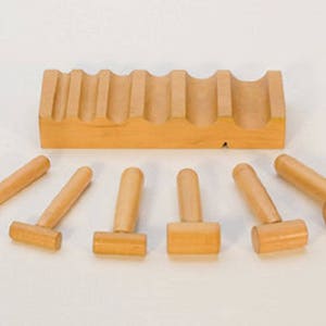 May include: A set of wooden mallets and a wooden rack. The mallets have a cylindrical handle and a rectangular or cylindrical head. The rack has multiple slots to hold the mallets. The items are made of light-colored wood.