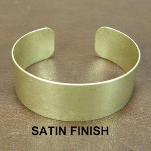 May include: A wide, satin-finished brass bangle bracelet. The bracelet is a simple, solid band with rounded edges.