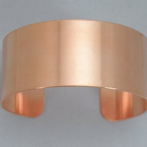 May include: A wide, copper cuff bracelet with a smooth, polished finish.