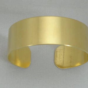 May include: A gold-colored metal cuff bracelet with a smooth, polished finish.