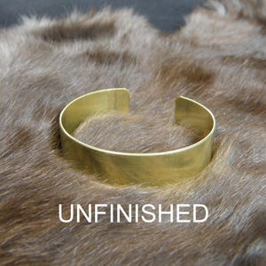 May include: Unfinished brass bangle bracelet. The bracelet is a simple, flat band with rounded edges.