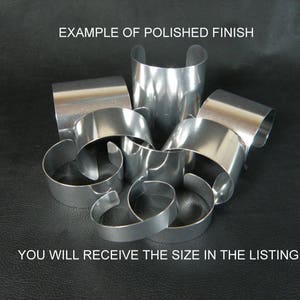 May include: A group of five silver metal bracelets with a polished finish. The bracelets are stacked on top of each other, showing the different sizes and shapes. The text "EXAMPLE OF POLISHED FINISH" is at the top of the image. The text "YOU WILL RECEIVE THE SIZE IN THE LISTING" is at the bottom of the image.