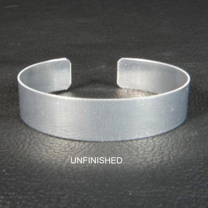 May include: Unfinished silver metal bracelet. The bracelet is a simple, flat band with rounded edges.