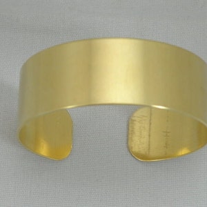 May include: A gold-colored metal cuff bracelet. The bracelet is smooth and has a simple design.