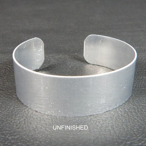 May include: Unfinished silver metal cuff bracelet. The bracelet is smooth and has a rounded shape.