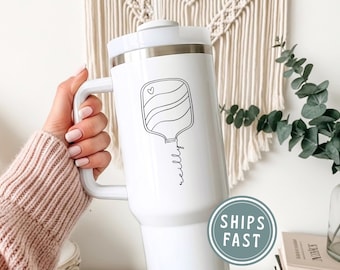 May include: White insulated tumbler with a handle and a lid. The tumbler features a black line drawing of a medical IV bag with a heart and the name "nelly" in script. The tumbler is designed for hot or cold beverages.