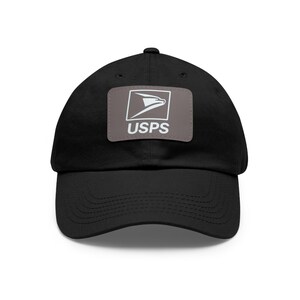 Puede incluir: Gorra de béisbol negra con visera curva. Un parche rectangular en la parte delantera muestra el logotipo de USPS y las letras "USPS" en blanco. La gorra está hecha de un material suave.