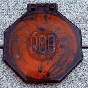May include: An octagonal, vintage compact mirror with a marbled orange and black design. The center features the etched number "888" within a circular frame. The compact has a dark brown, almost black, border and a clasp closure.