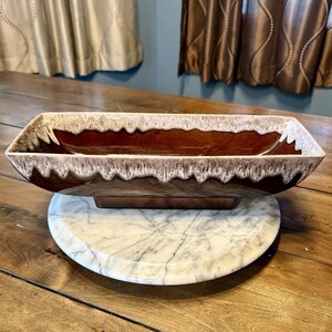 May include: A rectangular brown and white ceramic planter with a textured, dripped glaze design. The planter sits on a marble lazy susan, showcasing a mid-century modern aesthetic. The planter is approximately 16 inches long.