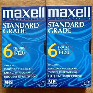 May include: Two Maxell VHS video cassette tapes. The blue boxes have the text "Maxell Video Cassette Standard Grade" and "6 Hours in EP Mode T-120". The boxes also have the text "VHS T-120/246m".