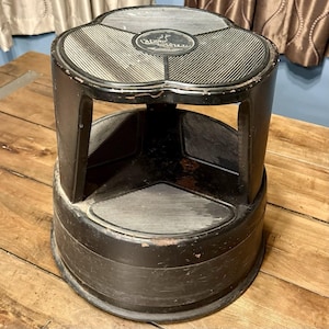May include: Black metal step stool with a textured, non-slip surface. The stool has a three-section top and a circular base. The brand name "Katzmaster" is visible on the top. The step stool is designed for reaching elevated areas.