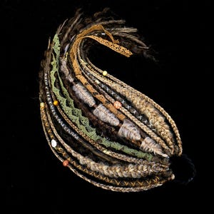 May include: A set of synthetic hair extensions featuring a mix of brown, tan, and grey dreadlocks and braids. The bundle is accented with green lace trim, tan ribbon, and various decorative beads in shades of yellow, red, and white.