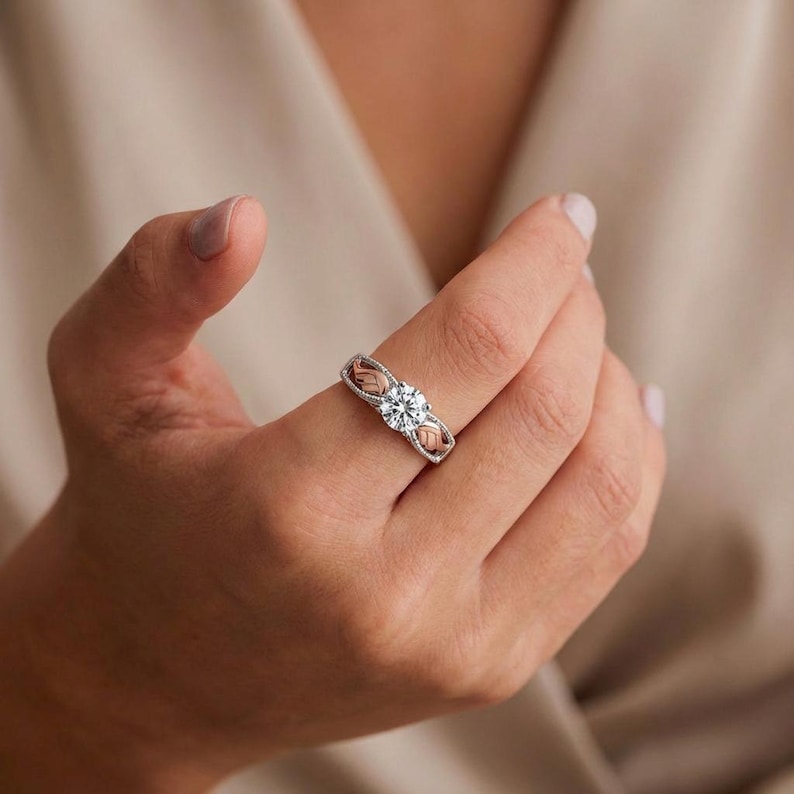 May include: A silver ring with a large, clear, round gemstone at the center. The ring has a delicate design with rose gold accents on either side of the central stone. The ring is on a person's finger.