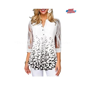 Puede incluir: Blusa blanca con cuello en V y mangas tres cuartos. La parte superior presenta un patrón circular en blanco y negro en la mitad inferior y mangas transparentes con un diseño decorativo. La blusa tiene una botonadura frontal.