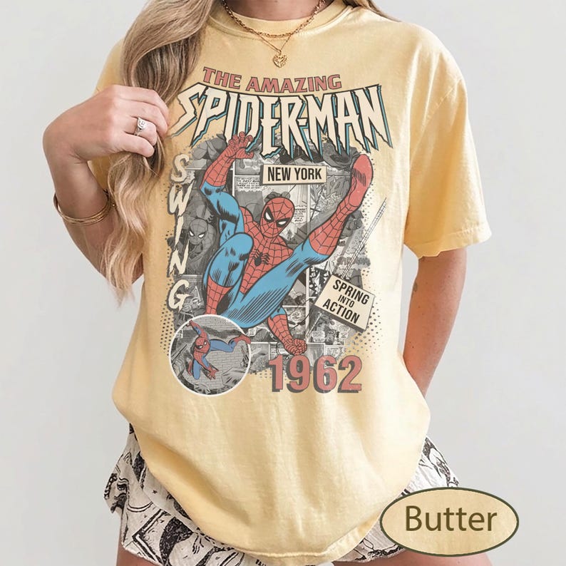 May include: Butter-colored t-shirt featuring a vintage comic book graphic of Spider-Man in action. The design includes the text "THE AMAZING SPIDER-MAN" and "1962". The shirt has short sleeves and a relaxed fit.