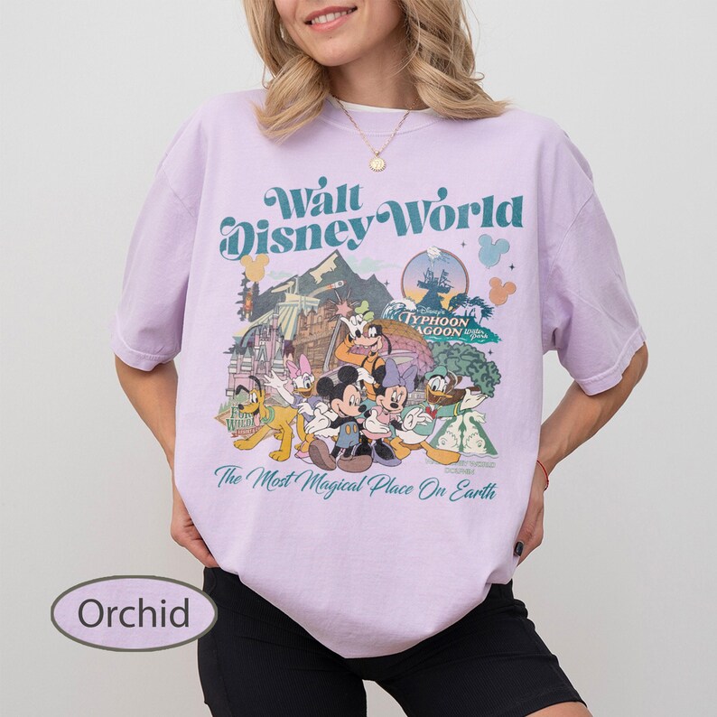 May include: Orchid-colored t-shirt featuring a vintage-style Walt Disney World graphic. The design includes various Disney characters and the text "The Most Magical Place On Earth". The shirt has short sleeves and a crew neck.