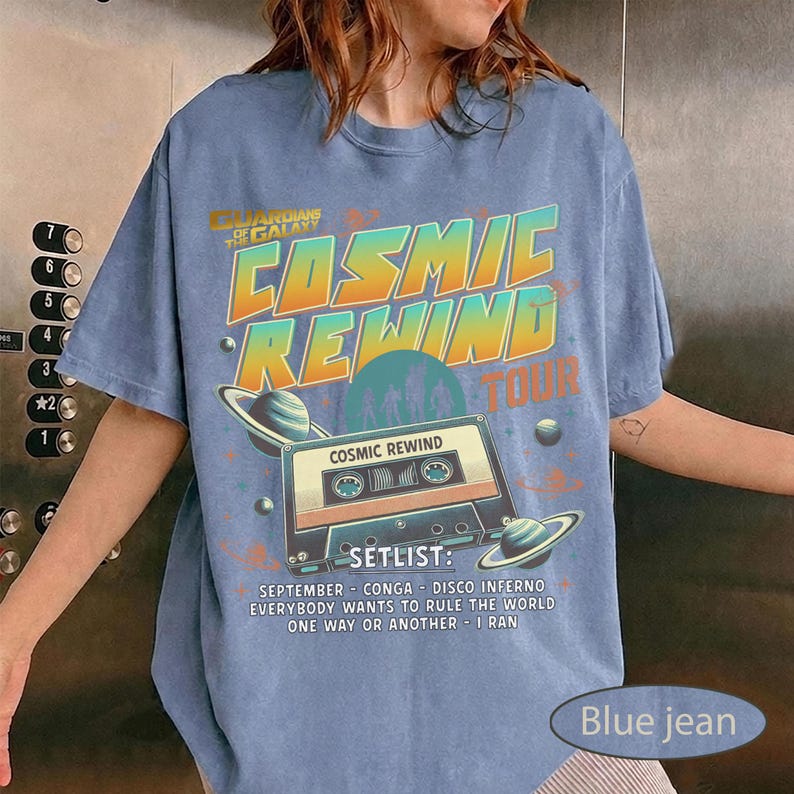 K&ouml;nnte beinhalten: Blaues Jeans-T-Shirt mit einem Grafikdesign, das die "Cosmic Rewind Tour" bewirbt. Das Design zeigt den Text "Guardians of the Galaxy" und "Cosmic Rewind Tour" in Orange und Blau. Eine Kassette und Planeten sind ebenfalls abgebildet.