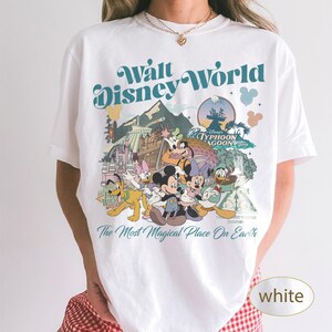 May include: White t-shirt featuring a colorful graphic of Disney characters and the text "Walt Disney World" and "The Most Magical Place On Earth". The design includes Mickey Mouse, Donald Duck, and Goofy.
