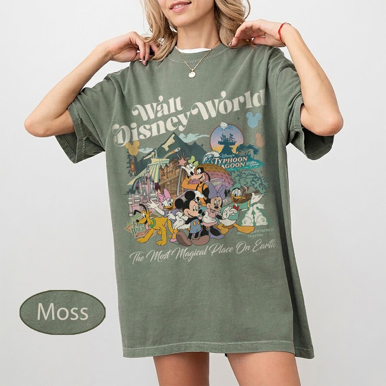 May include: Moss green t-shirt featuring a Walt Disney World graphic with Mickey Mouse, Donald Duck, and other characters. The shirt has the text "The Most Magical Place On Earth".