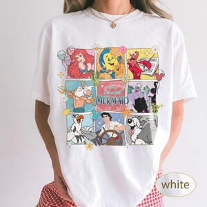 May include: White t-shirt with a colourful graphic of characters from Disney's The Little Mermaid. The design includes Ariel, Flounder, Sebastian, and other characters in a comic book style. The text "The Little Mermaid" is also present.