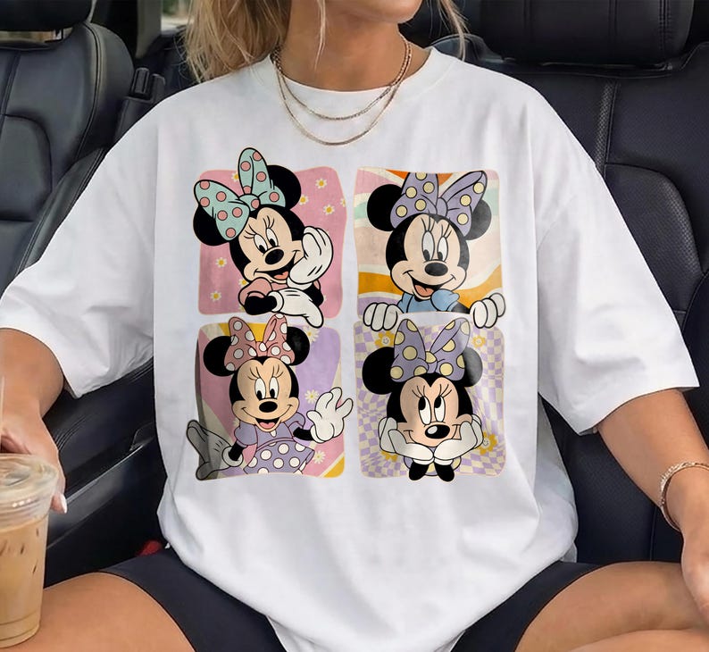 May include: White t-shirt featuring a colorful graphic of Minnie Mouse in four different poses. Each Minnie Mouse image is set against a unique background, including pink, orange, and purple hues. The shirt is a casual, oversized style.