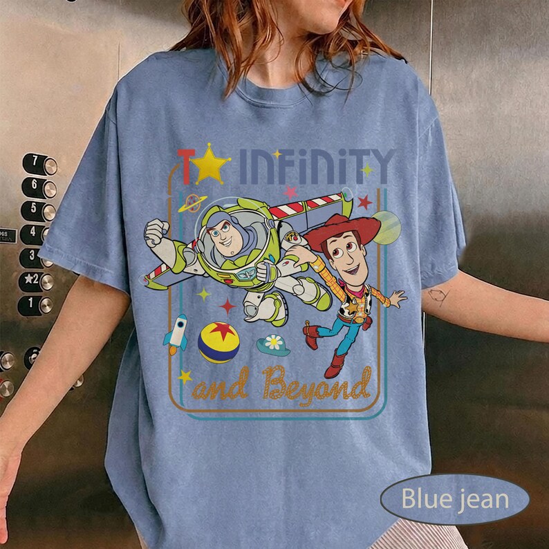 May include: Blue jean short-sleeve t-shirt featuring Buzz Lightyear and Woody from Toy Story. The shirt has the text "Infinity and Beyond" with a star and rocket ship graphic. The shirt is a light blue color.