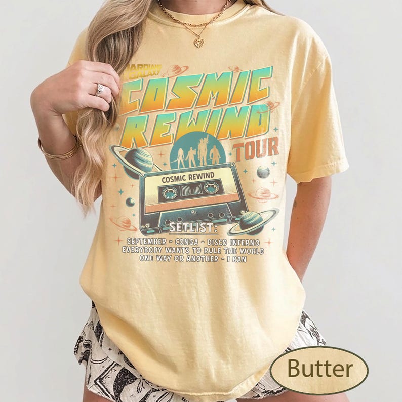 K&ouml;nnte beinhalten: Hellgelbes T-Shirt mit Retro-Grafik. Das Design enth&auml;lt den Text "COSMIC REWIND TOUR" und eine Kassettenillustration mit Planeten. Die Setlist umfasst: September, Conga, Disco Inferno, Everybody Wants to Rule the World, One Way or Another und I Ran.