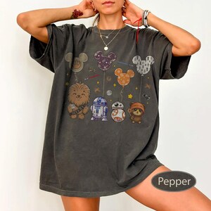 May include: Dark grey t-shirt featuring cartoon characters from Star Wars and Disney. The design includes Chewbacca, R2-D2, BB-8, and an Ewok, with Mickey Mouse-shaped balloons. The shirt is labeled "Pepper".