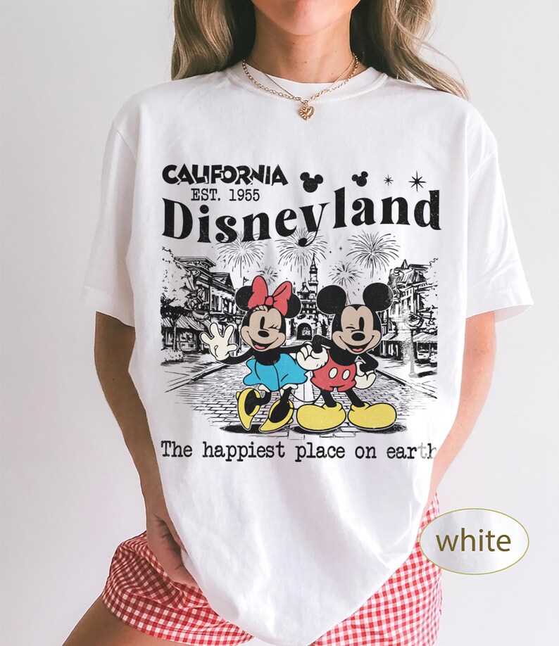May include: White t-shirt featuring a graphic of Mickey and Minnie Mouse in front of a Disneyland scene. The shirt has the text "CALIFORNIA EST. 1955 Disneyland" and "The happiest place on earth".