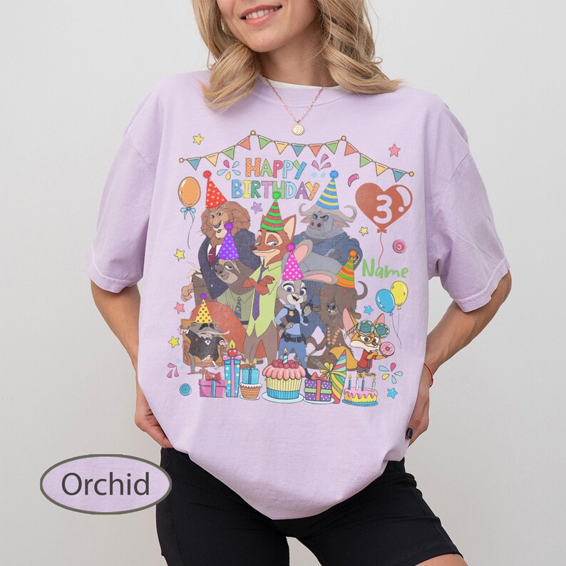 May include: Orchid-colored t-shirt featuring a colorful cartoon graphic with the text "Happy Birthday" and the number "3". The graphic includes various animal characters, balloons, and a birthday cake. The shirt is a comfortable, casual style.