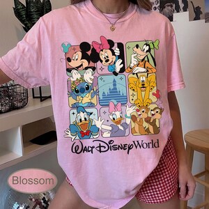 May include: A light pink t-shirt featuring a grid of Disney characters including Mickey Mouse, Minnie Mouse, Goofy, Stitch, Donald Duck, Daisy Duck, Chip and Dale. The words "Walt Disney World" are printed below the grid.