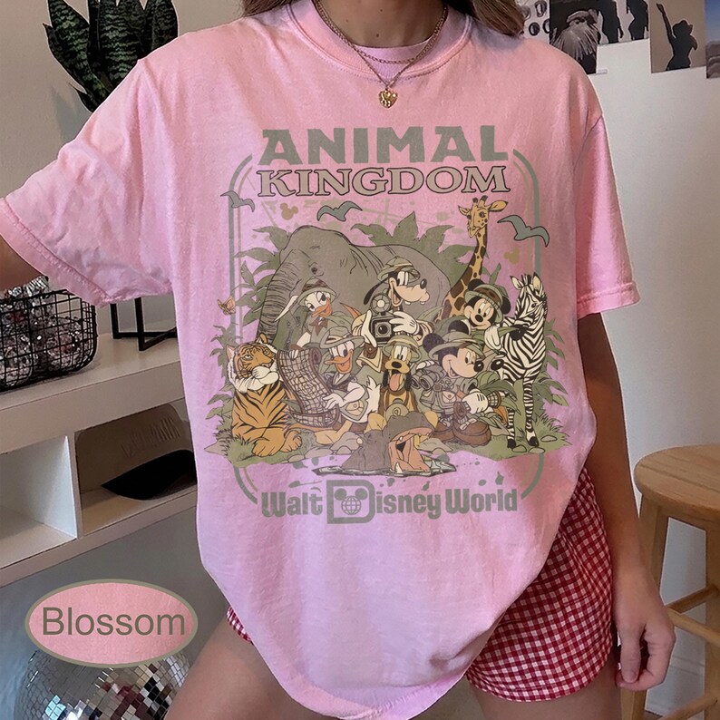 May include: Pink t-shirt with a graphic featuring Disney characters and the text "ANIMAL KINGDOM" and "Walt Disney World". The design includes an elephant, giraffe, zebra, tiger, and Mickey Mouse.