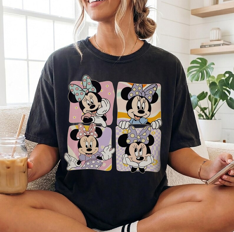 May include: Dark gray t-shirt featuring a four-panel design of Minnie Mouse in various poses. Each panel has a different background color and pattern, with Minnie wearing different outfits and bows. The shirt is a casual, oversized fit.