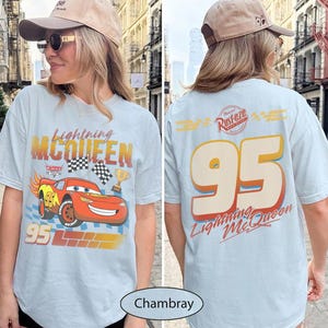 May include: Light blue t-shirt featuring Lightning McQueen from the Cars movie. The front graphic shows the character, checkered flags, and the number 95. The back displays the number 95, the text "Lightning McQueen", and the Rust-eze logo.